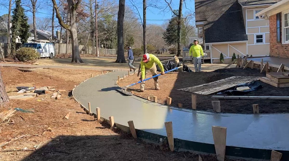 Crew screeding a fresh curved concrete walkway inside wood forms